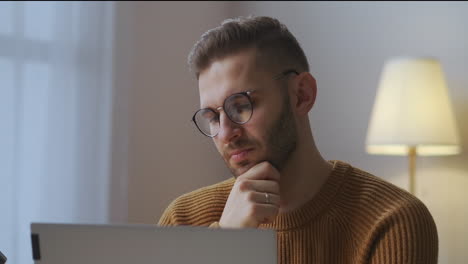 boring-man-with-glasses-is-listening-and-looking-at-screen-during-online-meeting-with-colleagues-sitting-at-home-nodding-head-portrait-of-male